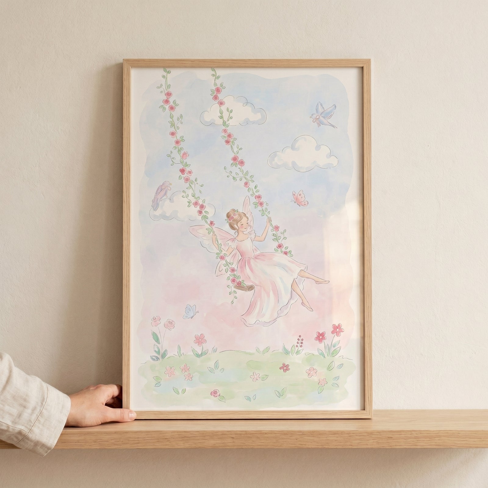 Framed rose swing fairy wall art shows a winged girl in a pink dress on a flower vine swing among soft clouds and birds.