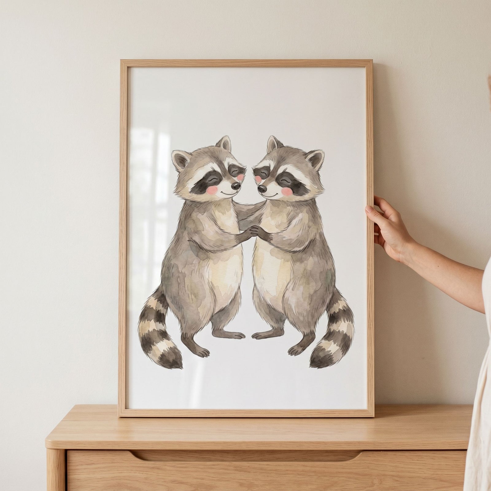 Rosy cheek dancing raccoons wall art featuring two watercolor animals holding hands in a light wood frame.