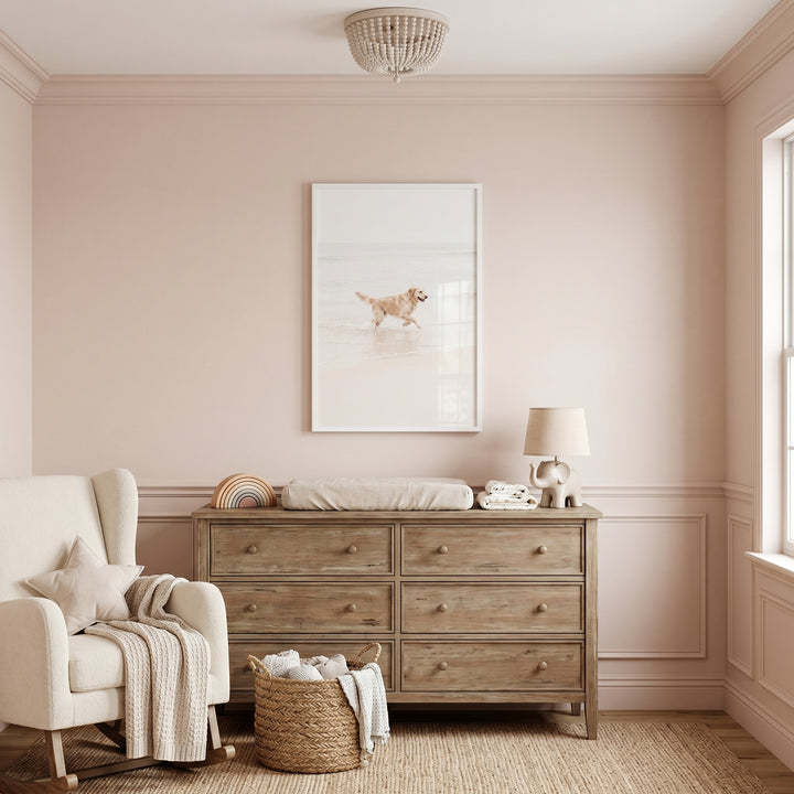 Pink nursery features a wood dresser, cream rocker, and running beach golden retriever wall art.