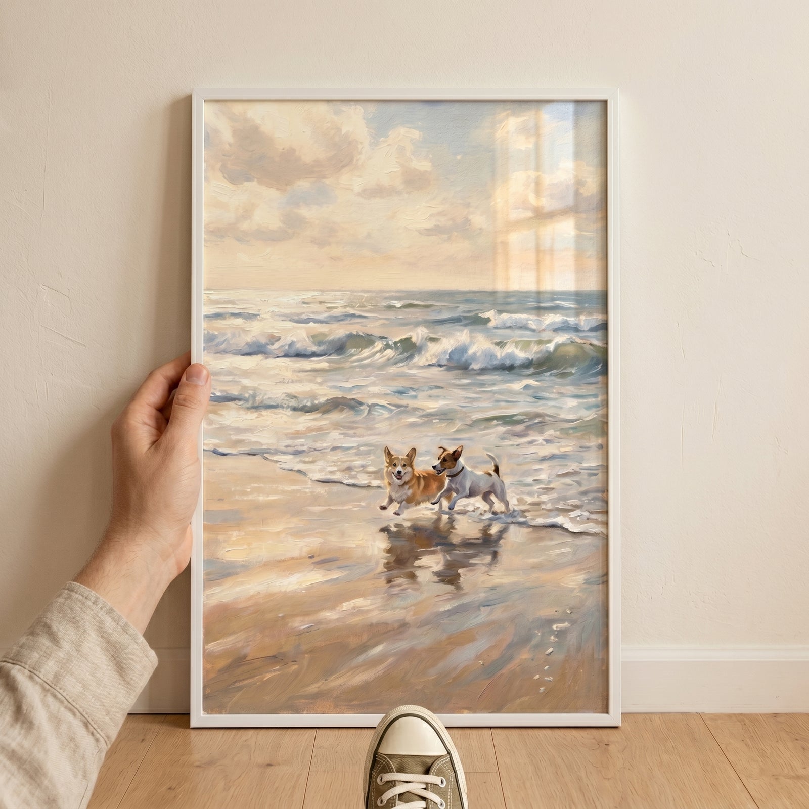 Two dogs splash in ocean waves on this framed running coastal beach corgi dog wall art held against a white wall.