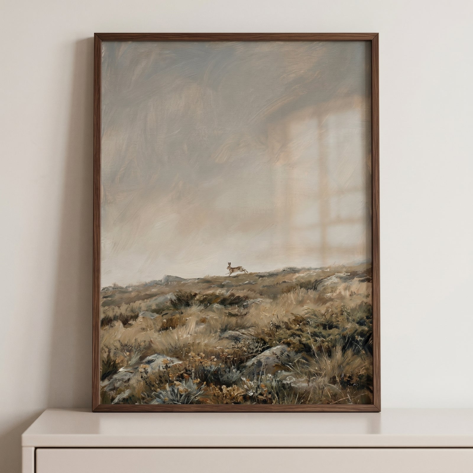 A hare leaps across a rocky, grassy landscape under a cloudy sky in this running moorland wild bunny wall art.
