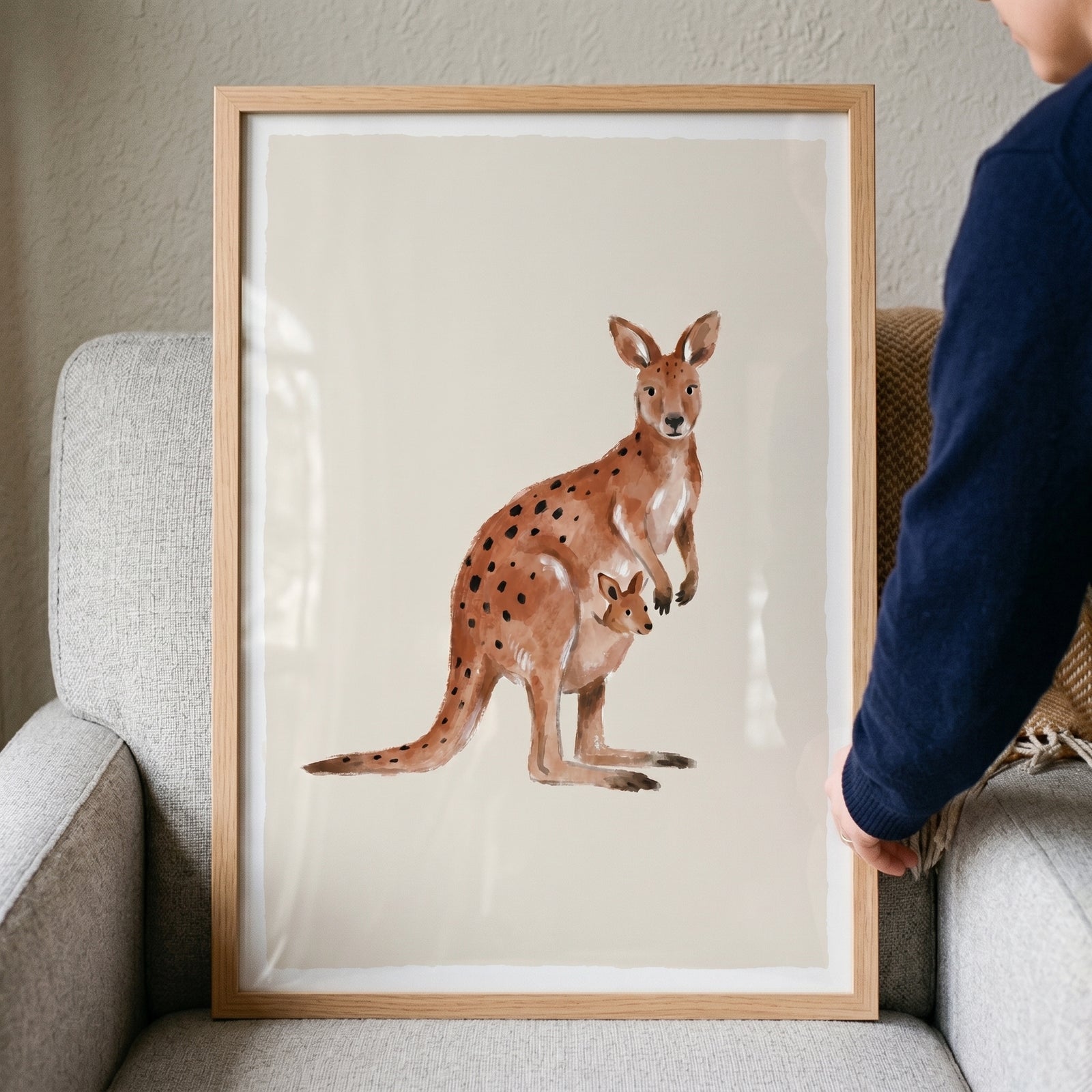 Rust spotted watercolor kangaroo wall art in a wooden frame featuring a mother and joey on a grey armchair.
