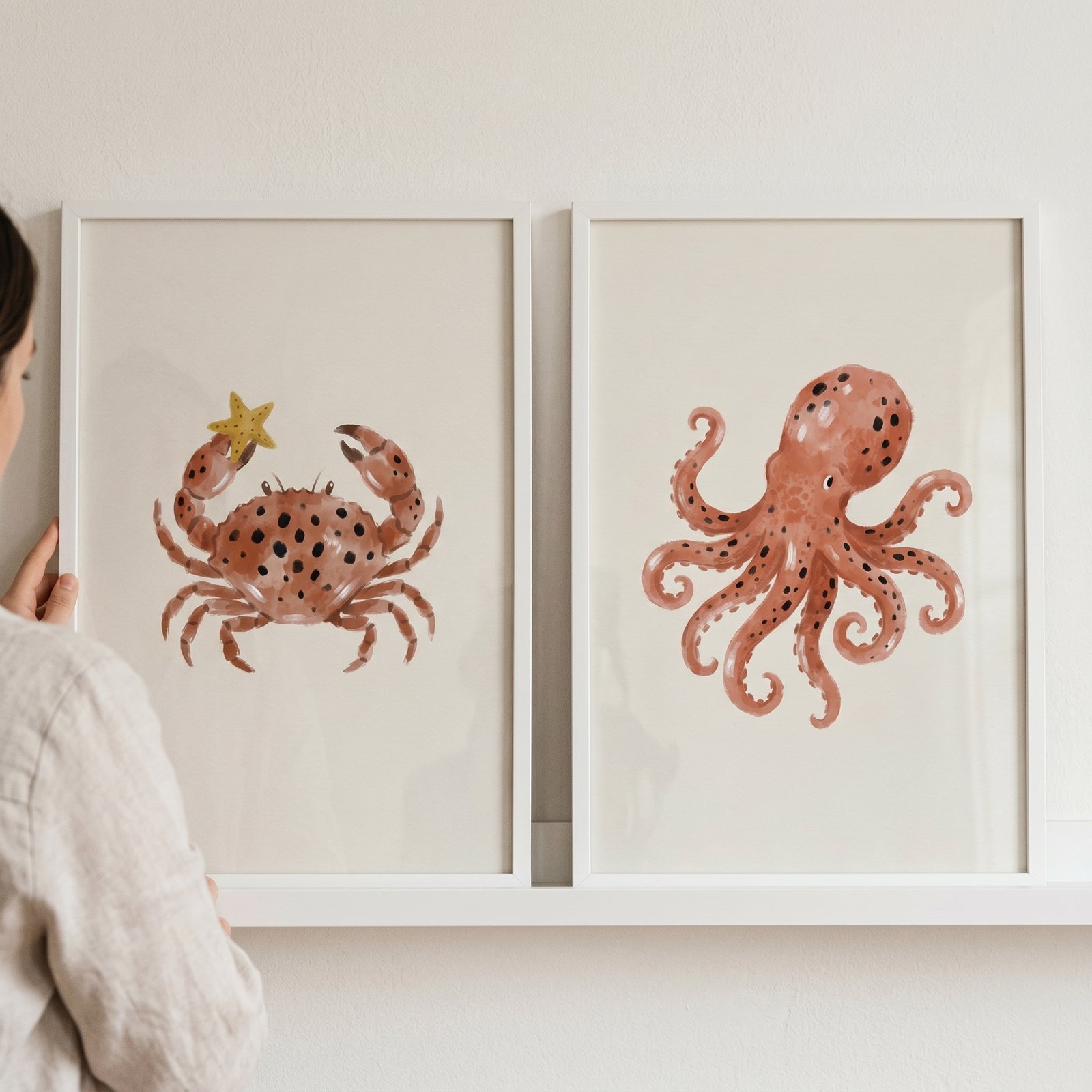 Rust watercolor sea animals wall art set of 2 featuring a spotted crab and octopus in white frames on a shelf.