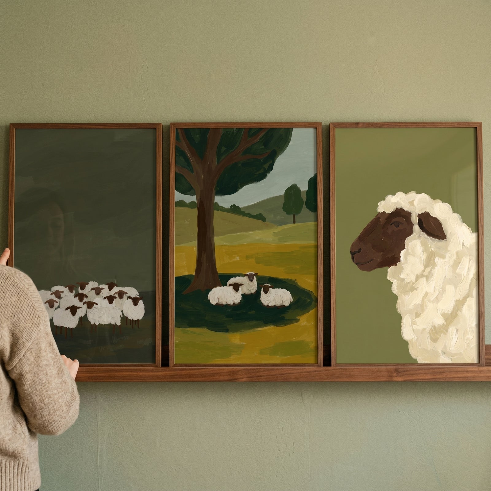 Rustic black face sheep wall art set of 3 framed prints displayed on a wooden shelf against a green wall.