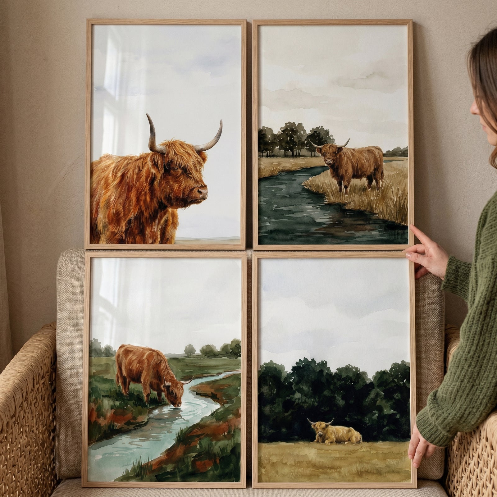 Rustic countryside highland cow wall art set of 4 framed illustrations held by a person in a green sweater.