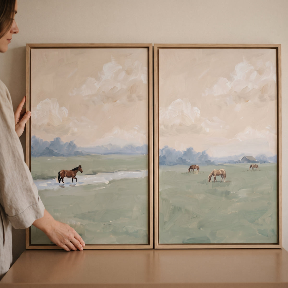 A rustic countryside meadow horse wall art set of 2 featuring horses in soft landscapes, held by a woman in a linen shirt.
