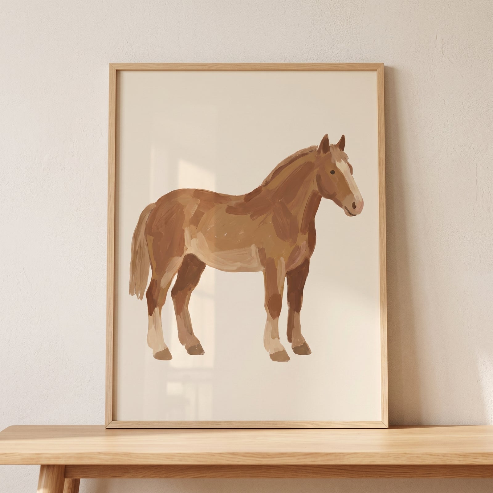 Rustic textured bay horse wall art in a light wood frame stands on a wooden table against a neutral wall.