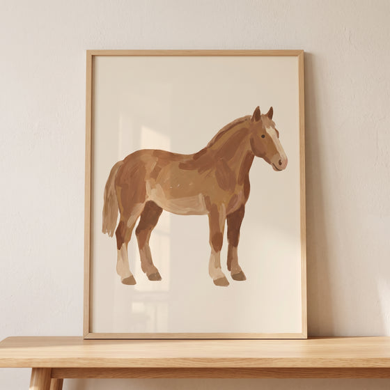 Rustic textured bay horse wall art in a light wood frame stands on a wooden table against a neutral wall.