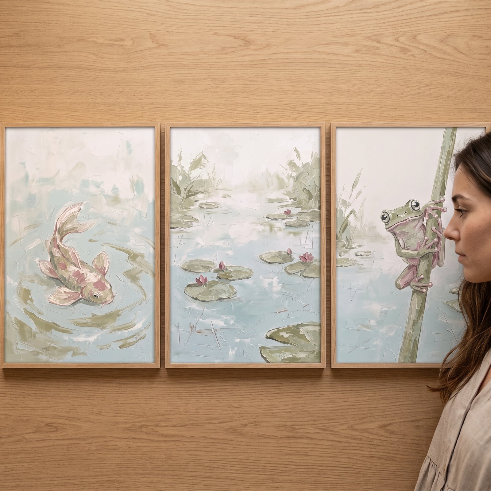 A woman views a sage green aquatic nature wall art set of 3 depicting a fish, lily pond, and frog on a wooden wall.