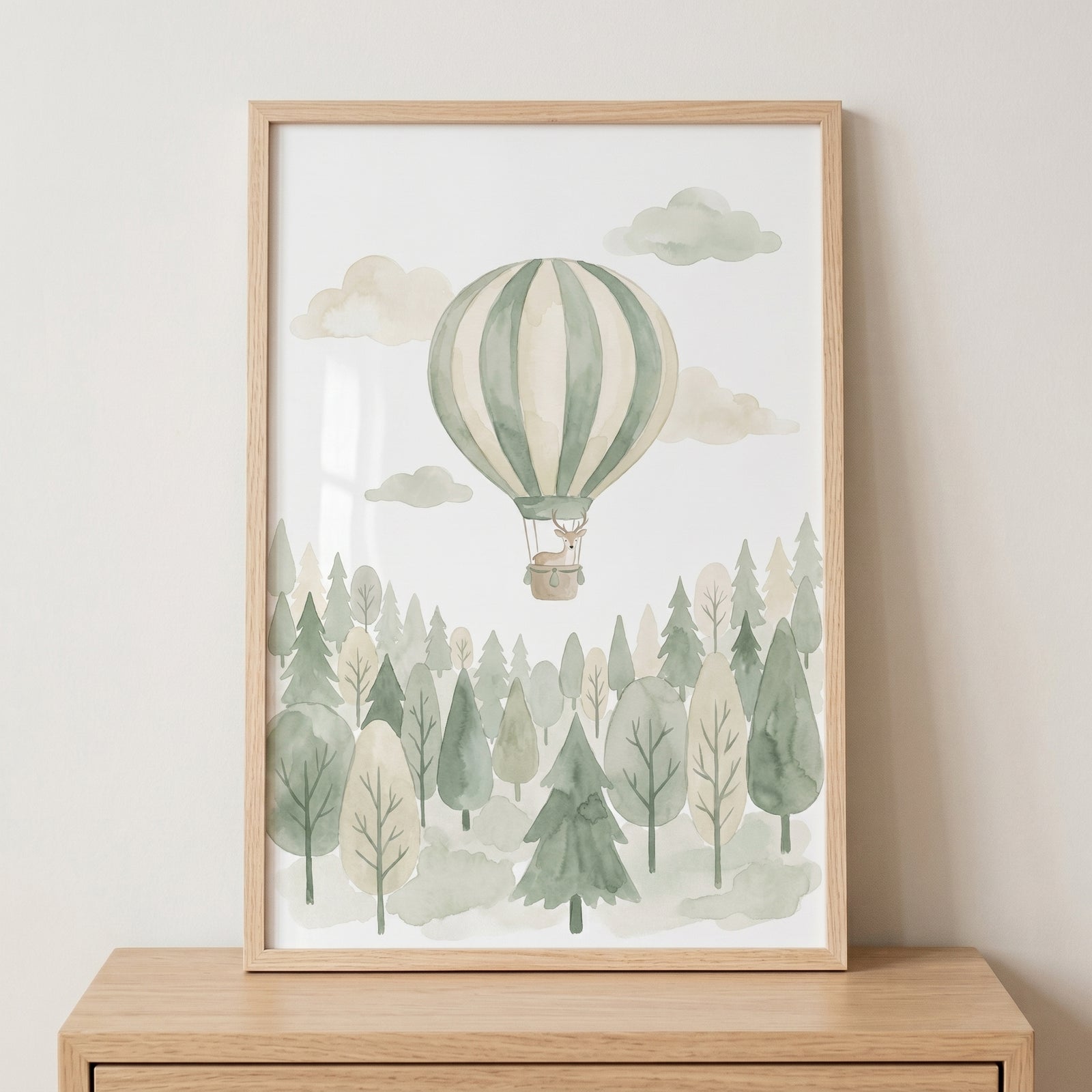 Sage green balloon deer artwork in a wood frame features a deer in a hot air balloon over a watercolor forest.