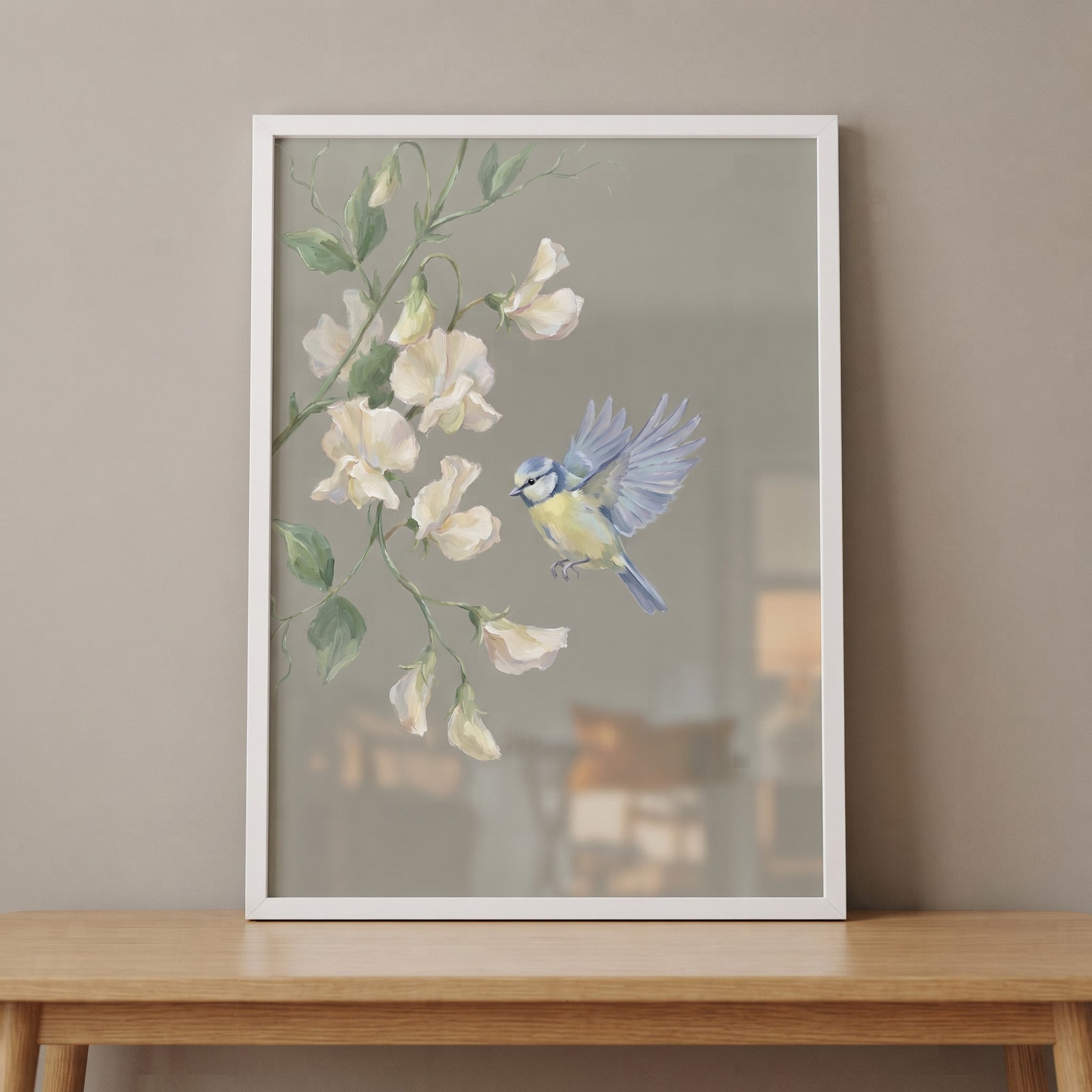 Sage green botanical bird floral wall art with a blue bird flying toward white flowers in a white frame on a table.