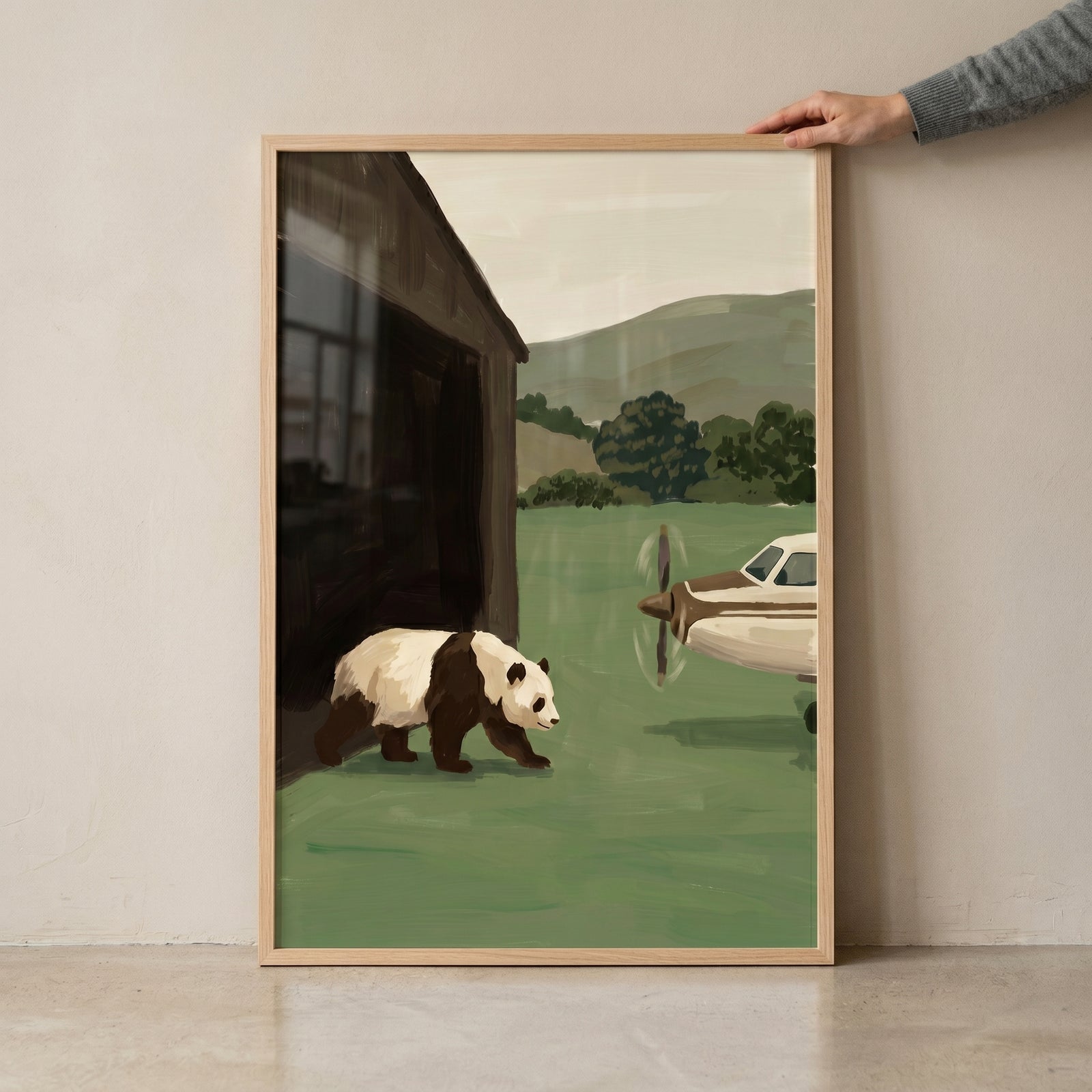 A panda walks past a small airplane and a wooden building in this sage green landscape panda artwork.