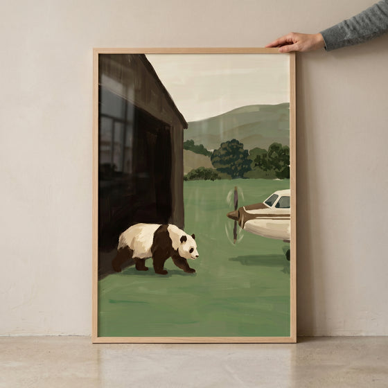 A panda walks past a small airplane and a wooden building in this sage green landscape panda artwork.