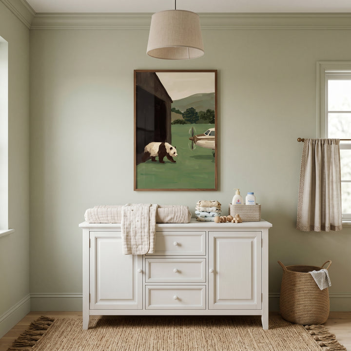 White dresser sits below sage green landscape panda artwork in a room with light green walls, a beige lamp, and a jute rug.