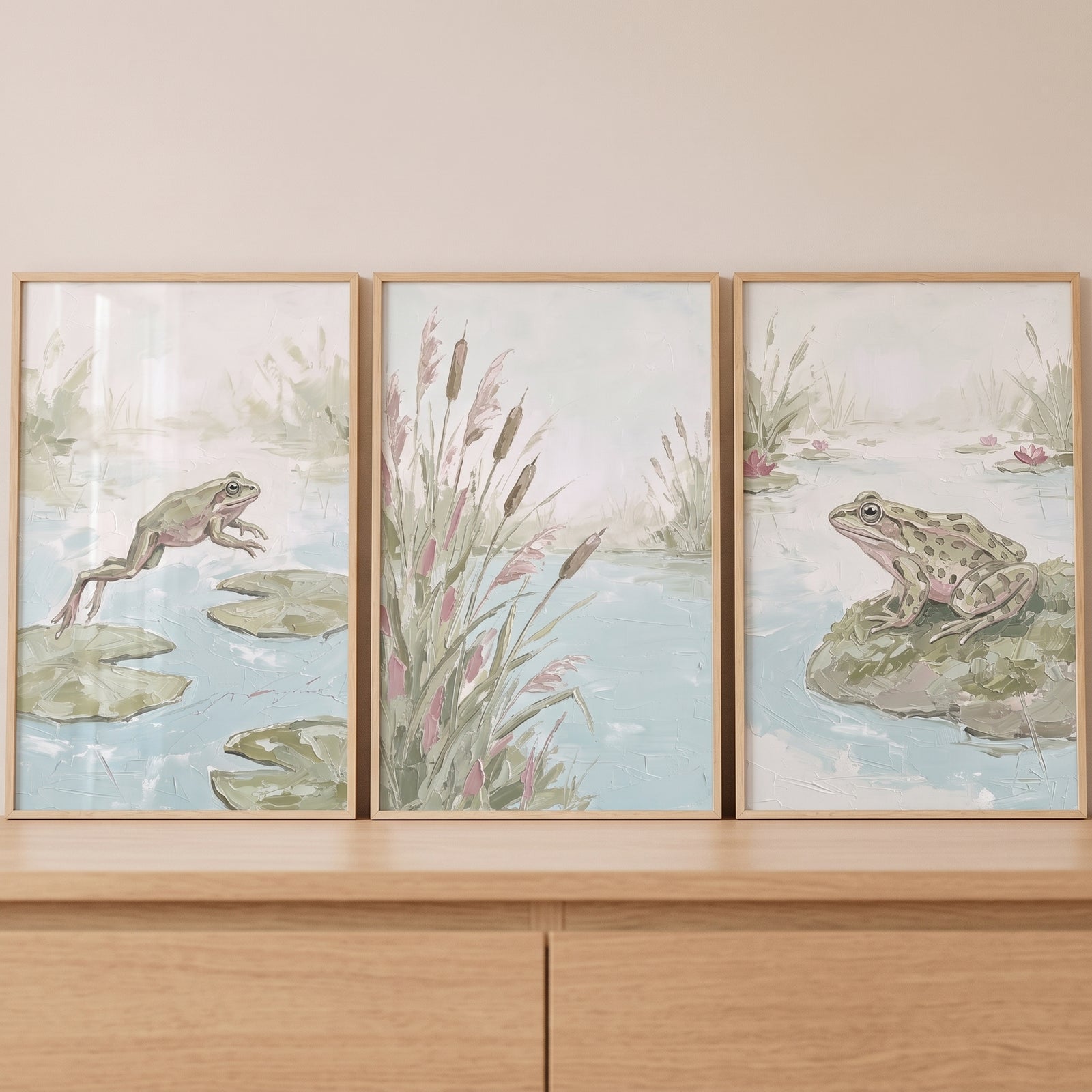 Sage green marshland pond wall art set of 3 features frogs jumping and sitting among reeds in light wood frames.