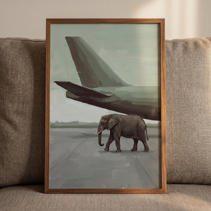 Sage green runway elephant wall art of an elephant walking under an airplane tail, in a wooden frame on a gray couch.
