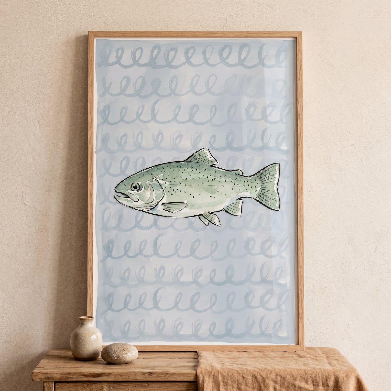 Sage green spotted trout fish wall art in a wooden frame displayed on a wooden table with small ceramic objects.