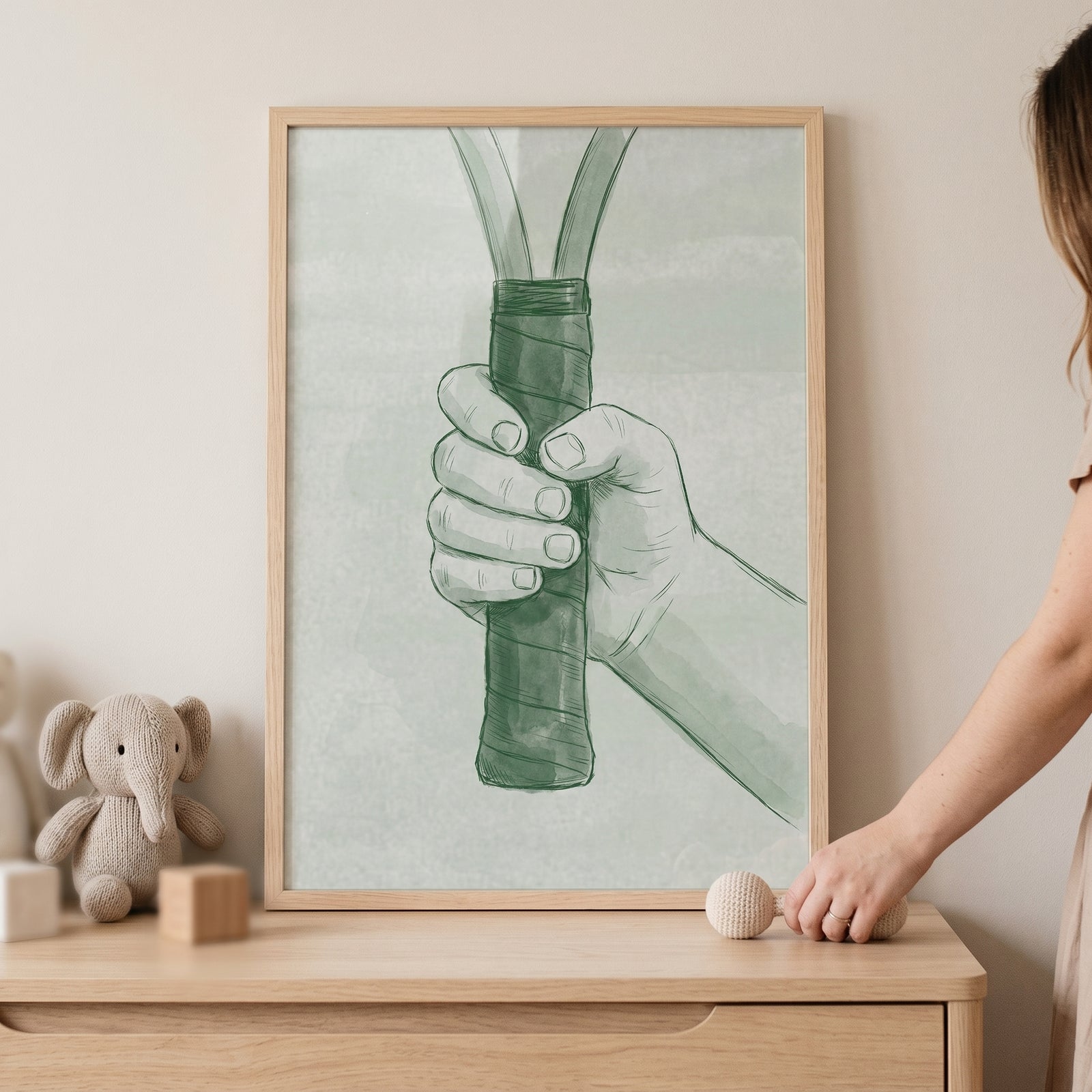 Framed sage green tennis wall art showing a hand gripping a racket above a wooden dresser with a plush elephant.