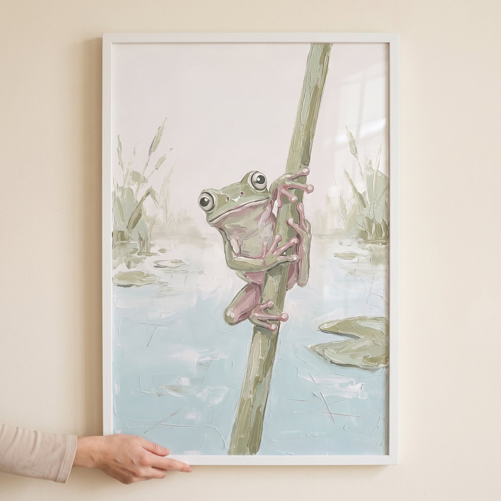 Sage green tree frog wall art depicts a wide-eyed frog climbing a reed in a pond, held in a white frame.