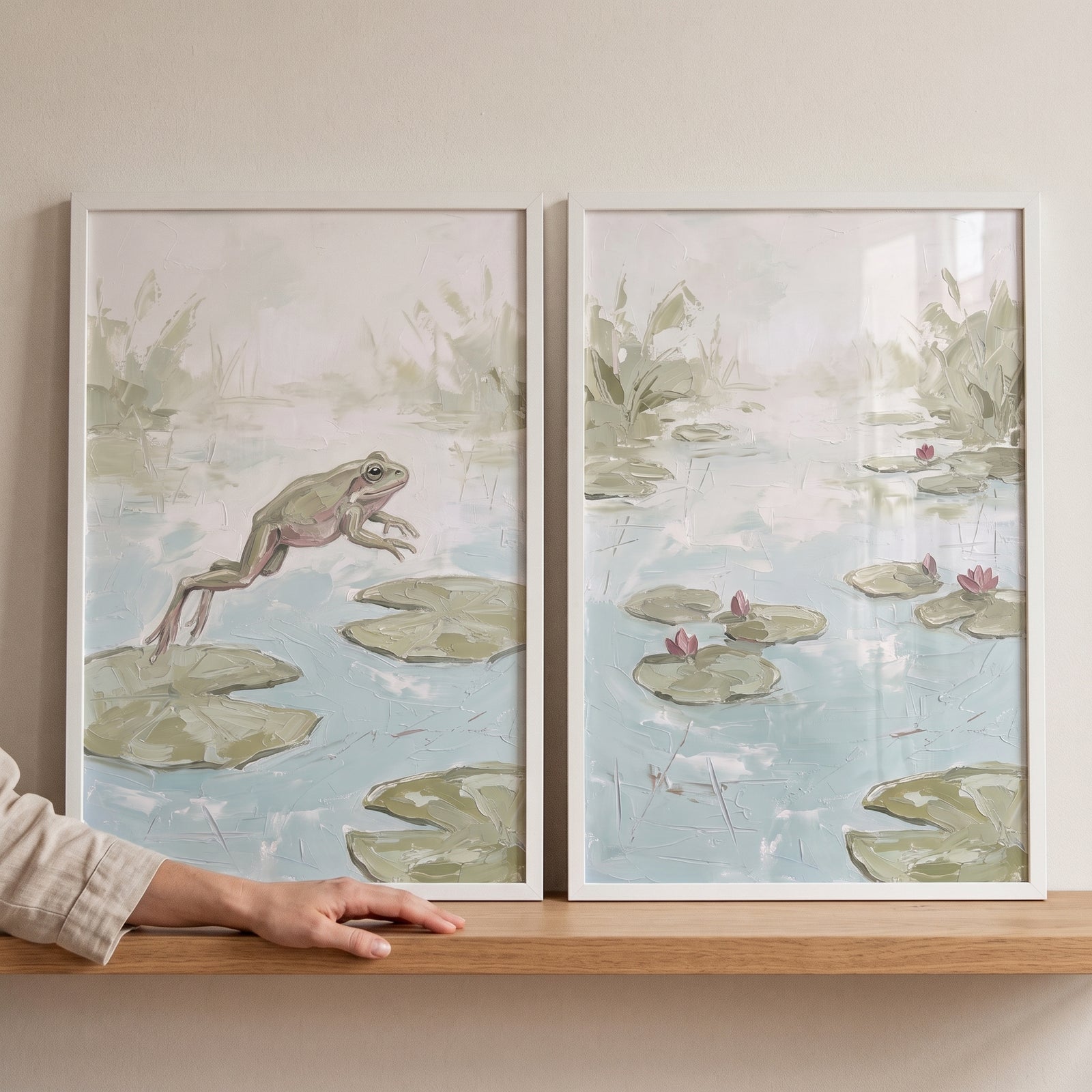 Sage lily pad frog wall art set of 2 in white frames on a wooden shelf, featuring a jumping frog and a serene lily pond.