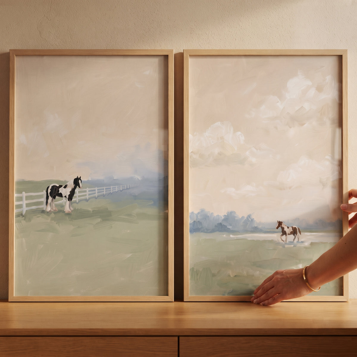 Sage meadow pinto horse wall art set of 2 in wood frames shows horses in soft green fields. A hand touches the frame.
