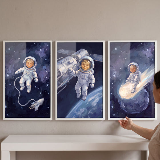 Sapphire starry baby astronaut wall art set of 3 depicts a toddler in spacesuits near a rocket, satellite, and a comet.