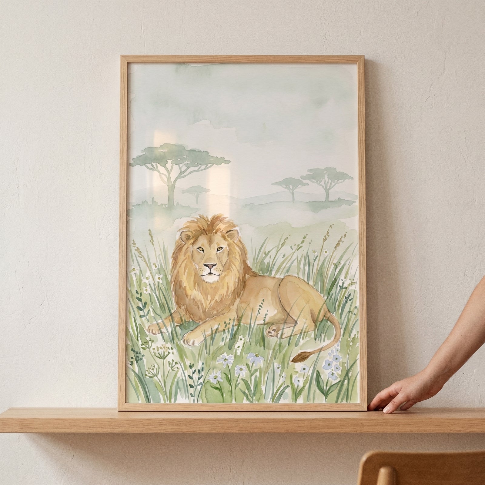 Framed savanna meadow lion wall art on a wooden shelf depicts a lion resting in tall grass with acacia trees behind.