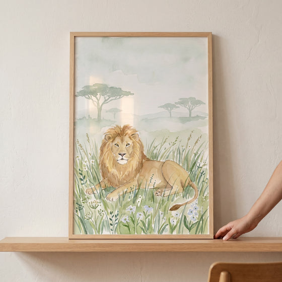 Framed savanna meadow lion wall art on a wooden shelf depicts a lion resting in tall grass with acacia trees behind.
