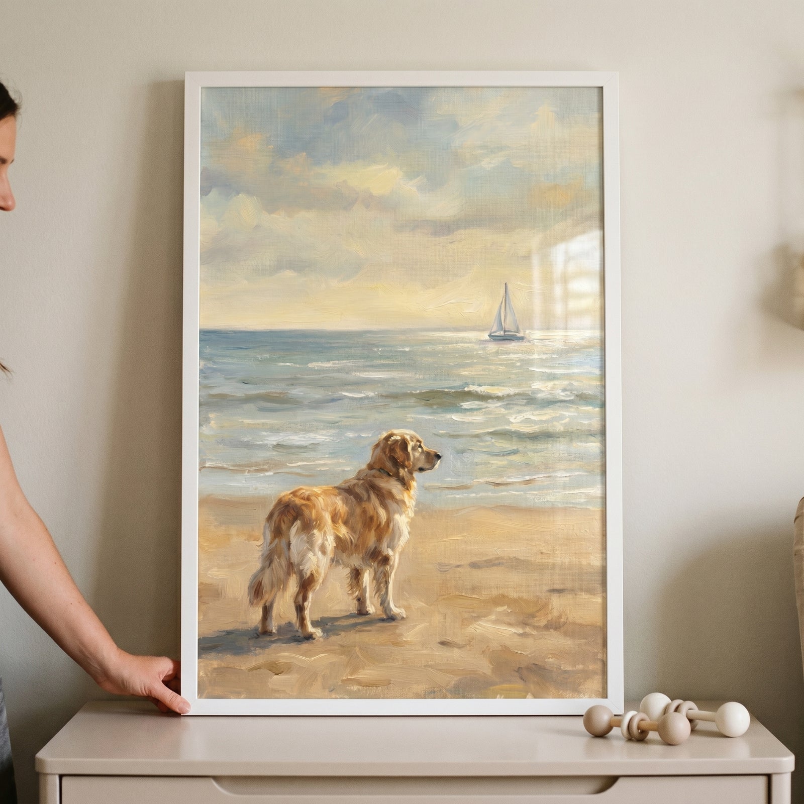 Scenic coastal golden retriever dog wall art in a white frame shows a dog on a beach looking at a sailboat on the ocean.
