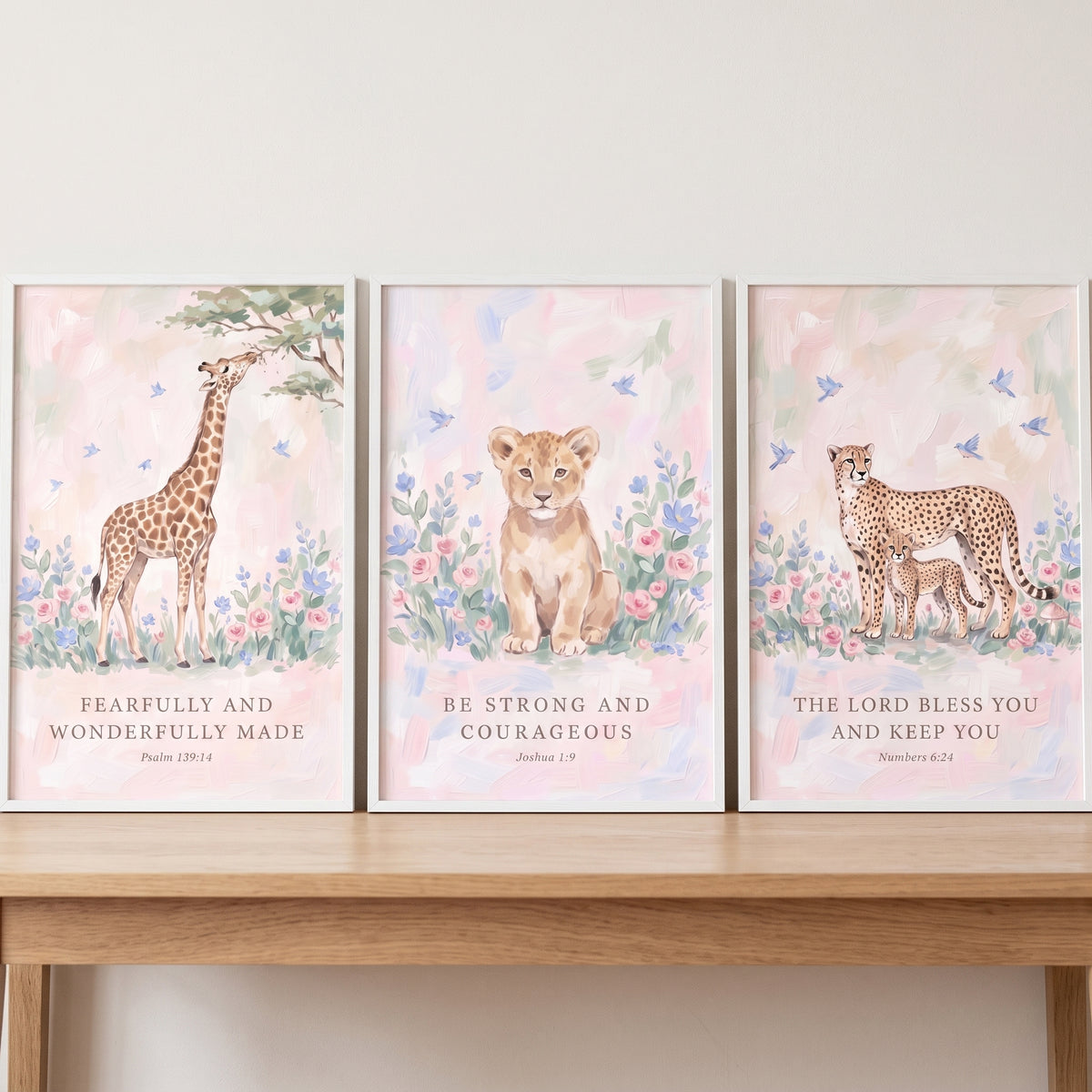 Scripture blush wildflower animals wall art set of 3 with a giraffe, lion cub, and cheetah on a wooden shelf.