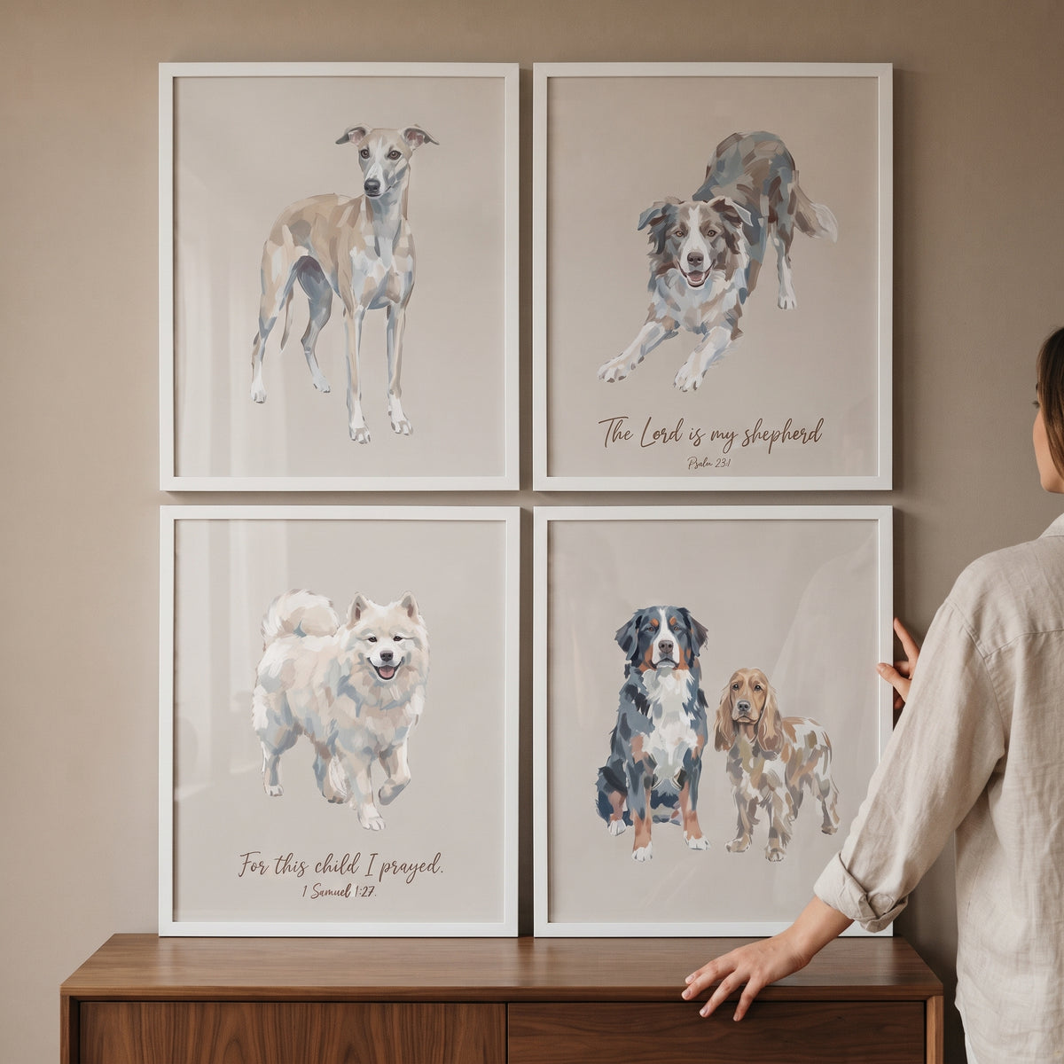 A person hangs scripture inspired beige dog artwork set of 4 in white frames above a wooden dresser.