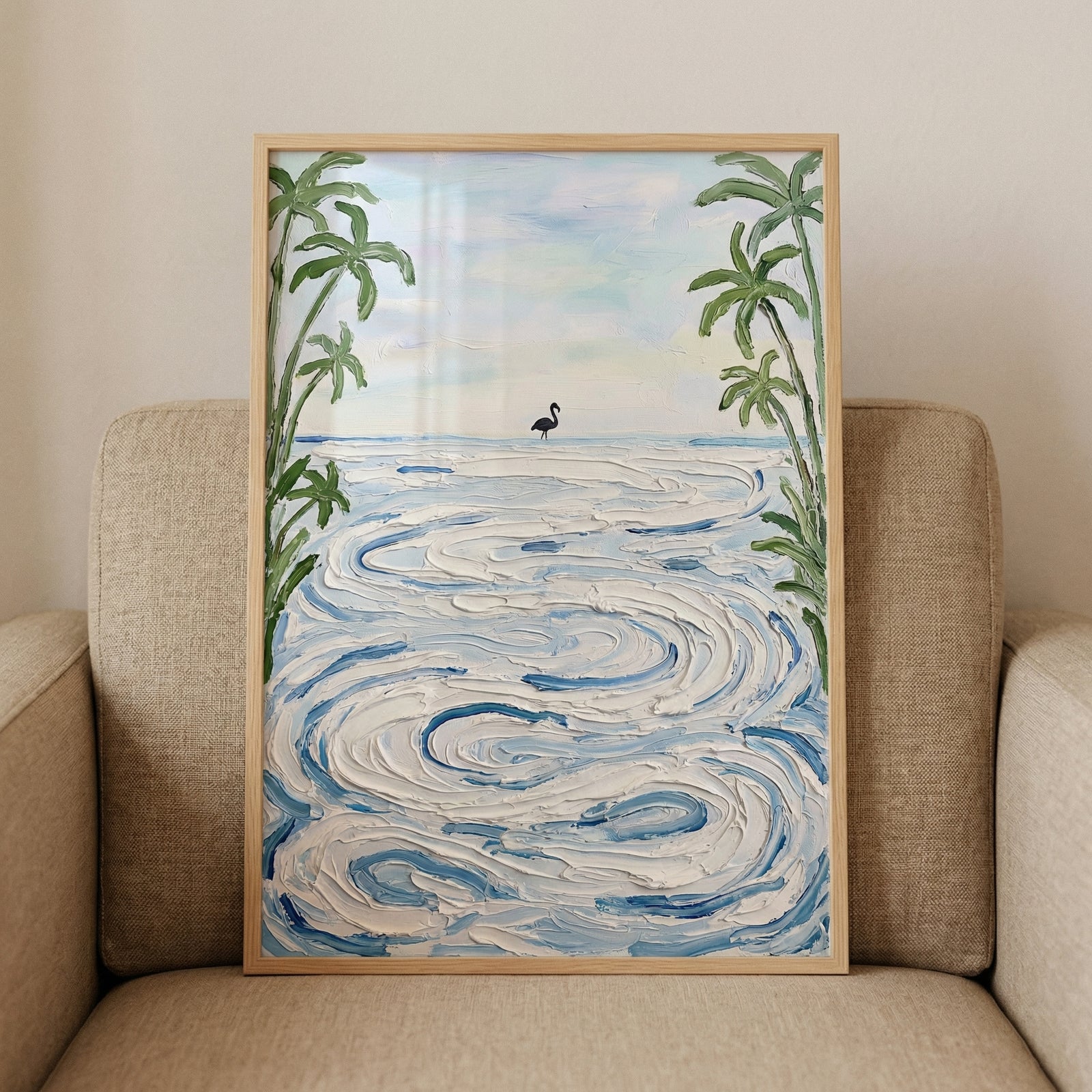 Framed painting of a calm ocean scene with textured swirling waves and a small bird standing near the shoreline framed by tall palm trees. The artwork rests against a cushioned chair highlighting its soft coastal colors and peaceful beach atmosphere.
