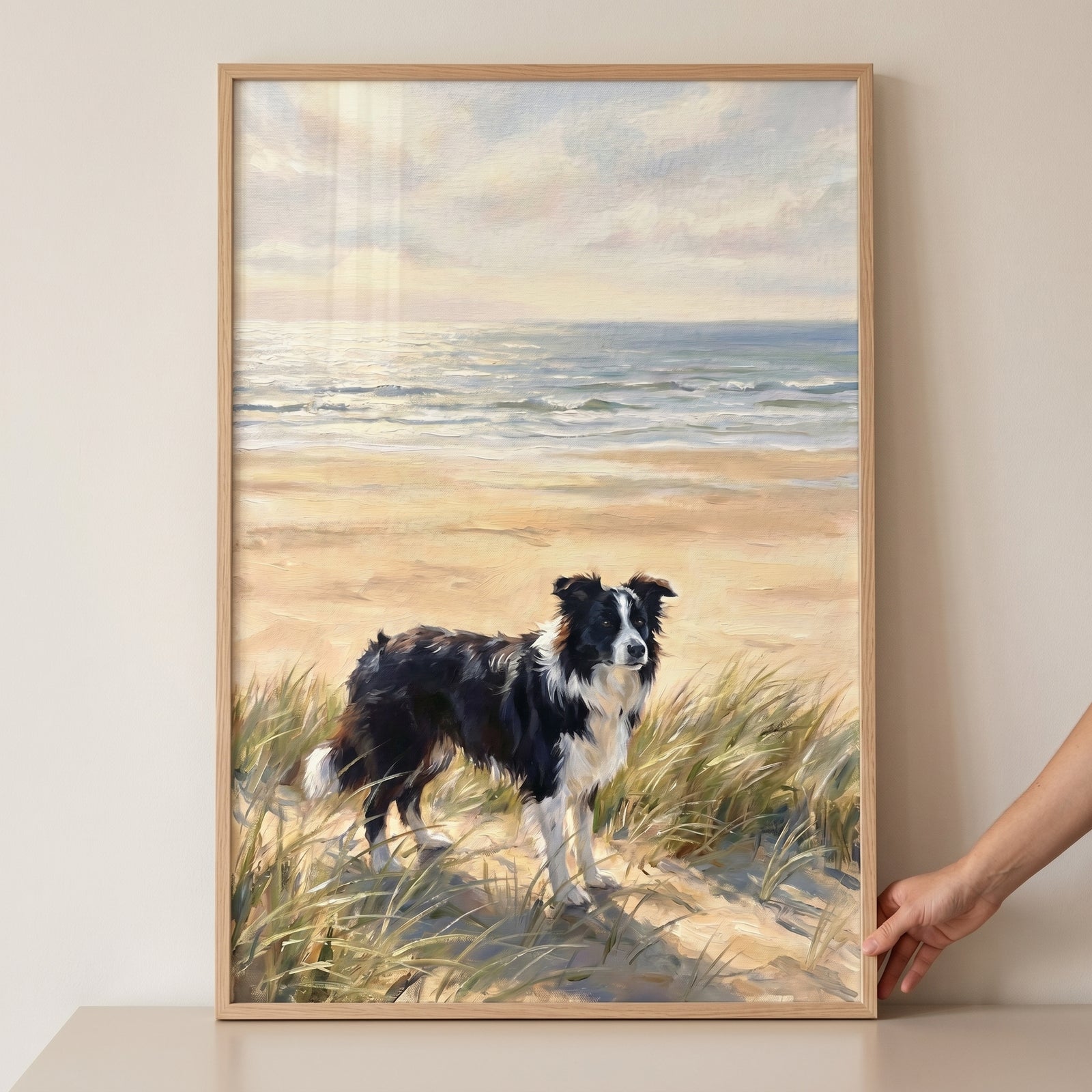 Hand holding sea grass dunes border collie dog artwork showing a black and white dog on a beach under a sunset sky.