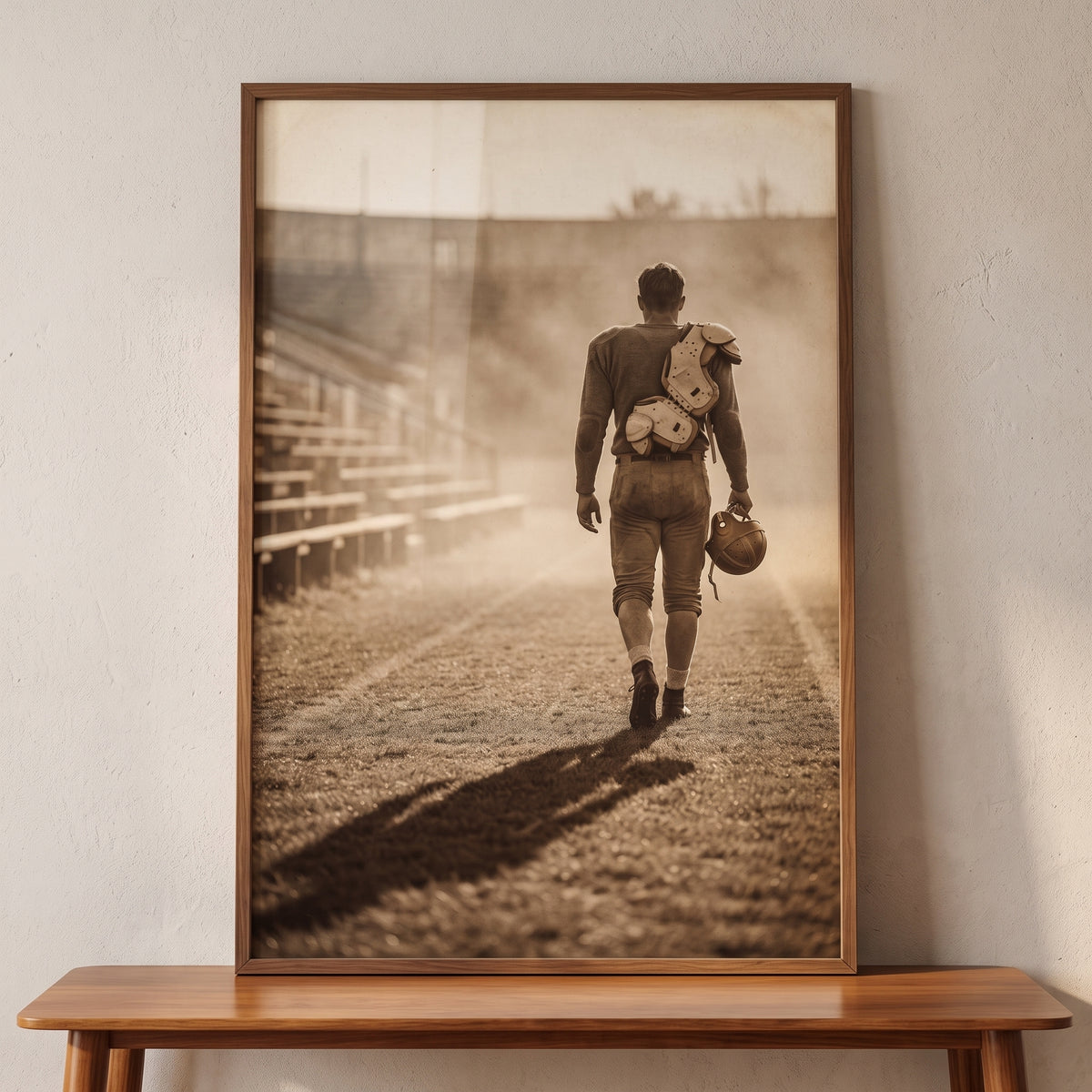 Sepia vintage football player sports wall art shows an athlete walking across a field, framed and set on a wooden table.