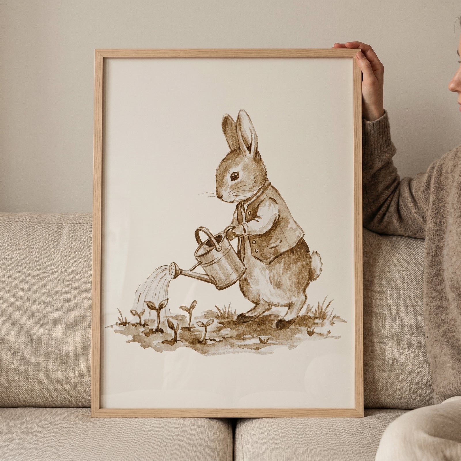 Framed sepia watercolor gardening bunny wall art shows a rabbit in a vest watering sprouts with a metal can.