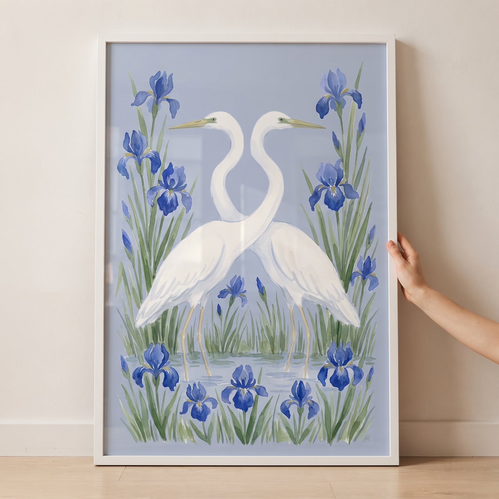 Two white birds with necks crossed among blue irises in this serene aquatic floral egret bird wall art in a white frame.