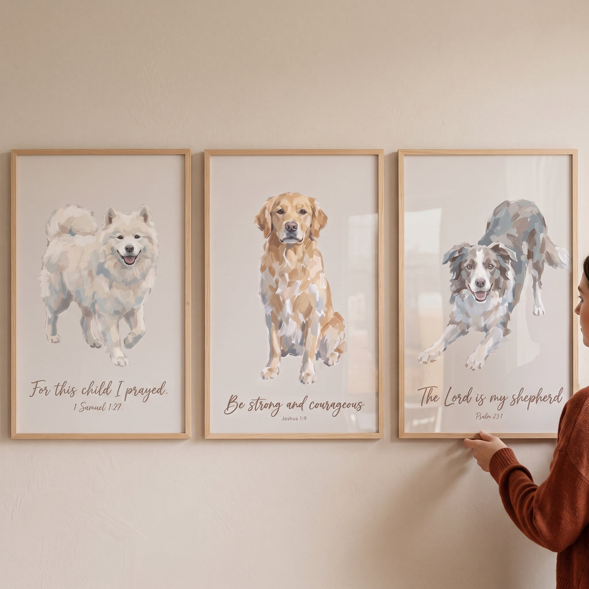 A person hangs a serene bible verse dogs wall art set of 3 with wood frames and dog illustrations on a neutral wall.