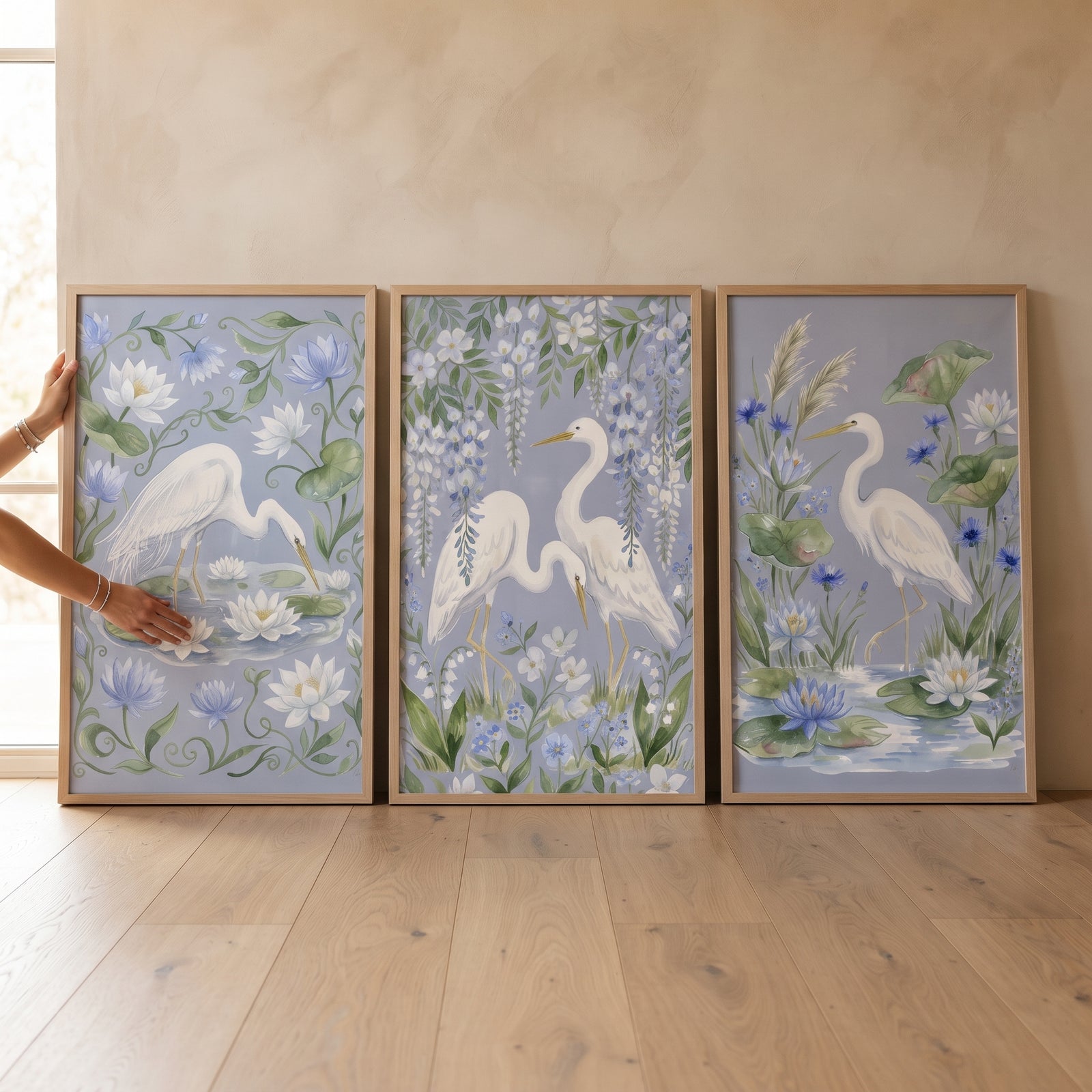 Serene botanical white egret bird wall art set of 3 with white herons and blue flowers on a wood floor.