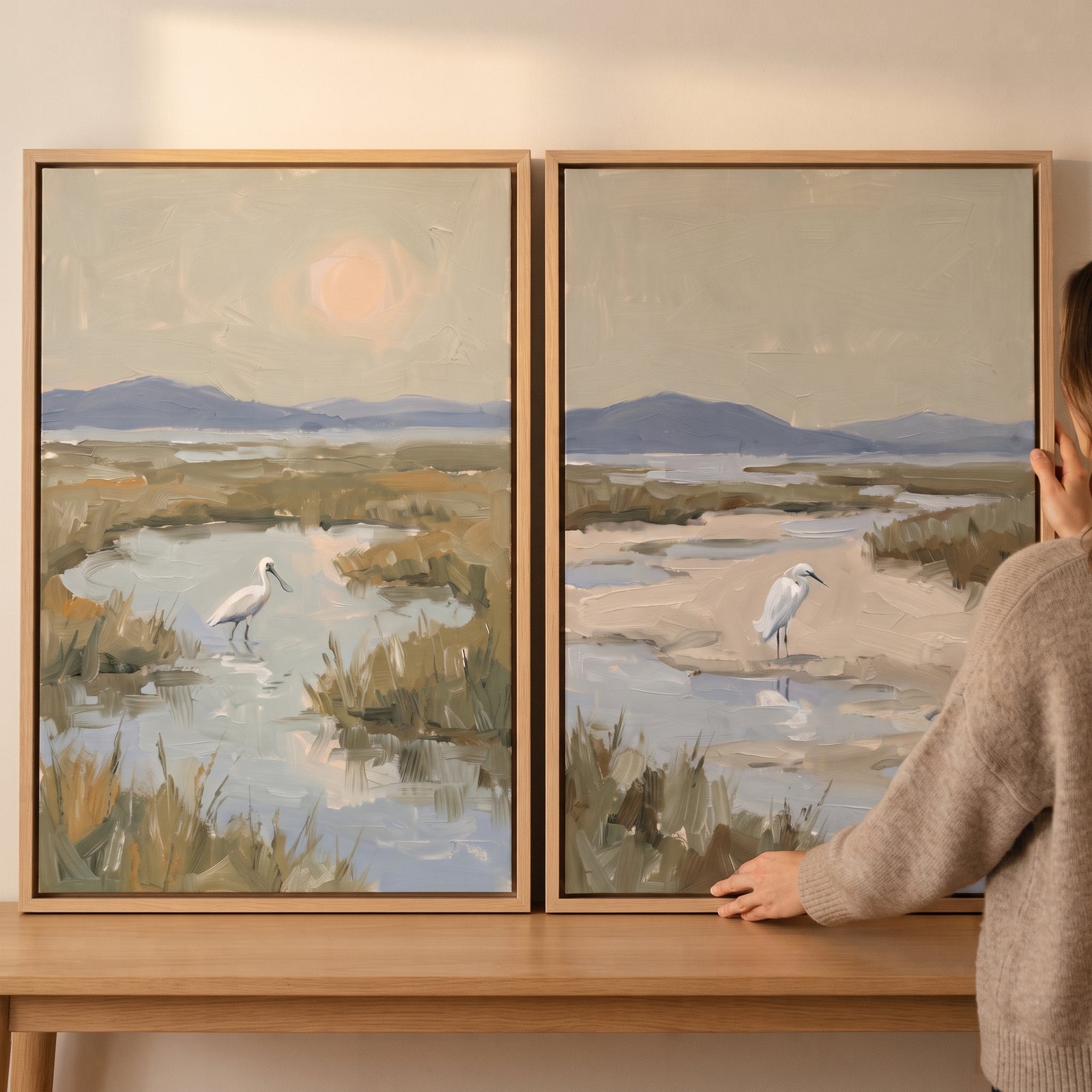 Person holding a serene coastal white bird wall art set of 2 showing birds in a marshy landscape with hills.