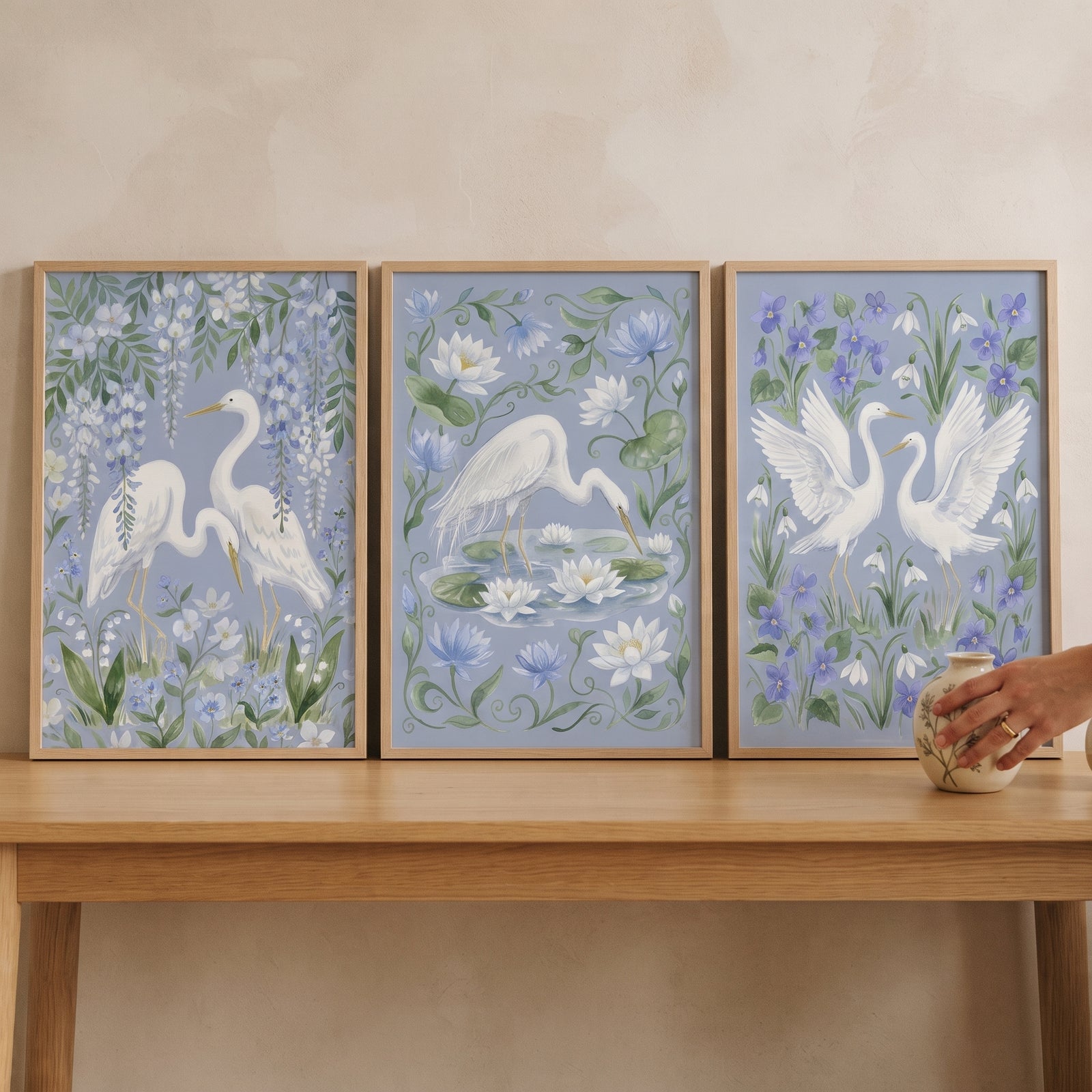 Serene coastal white egret bird wall art set of 3 featuring birds and lilies in frames on a light wood console table.