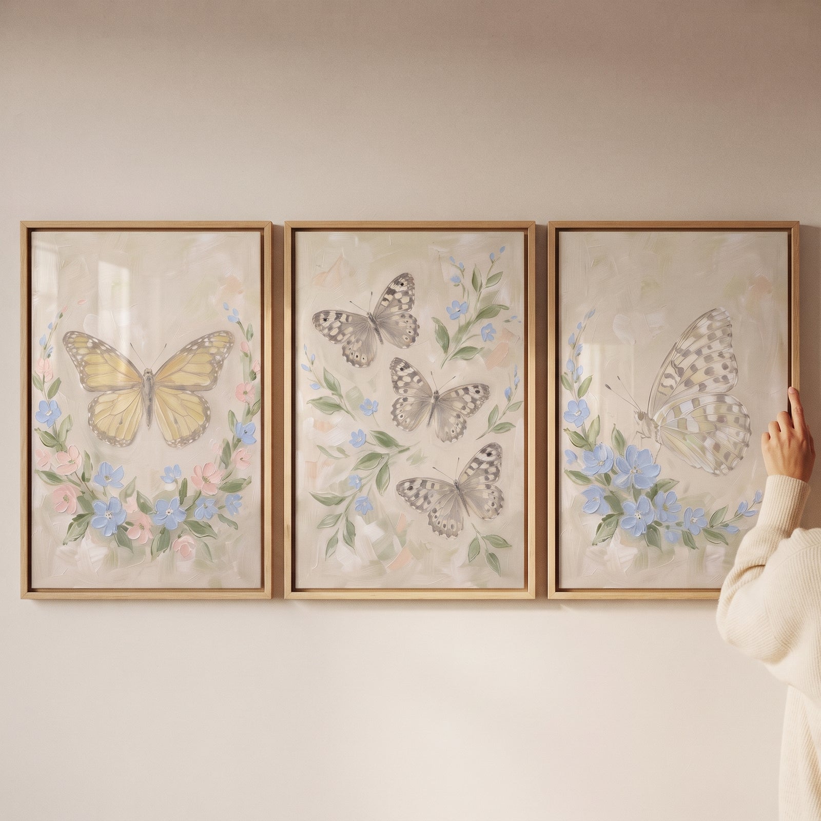 A hand adjusts a serene garden butterfly wall art set of 3 with soft pastel florals and butterflies.