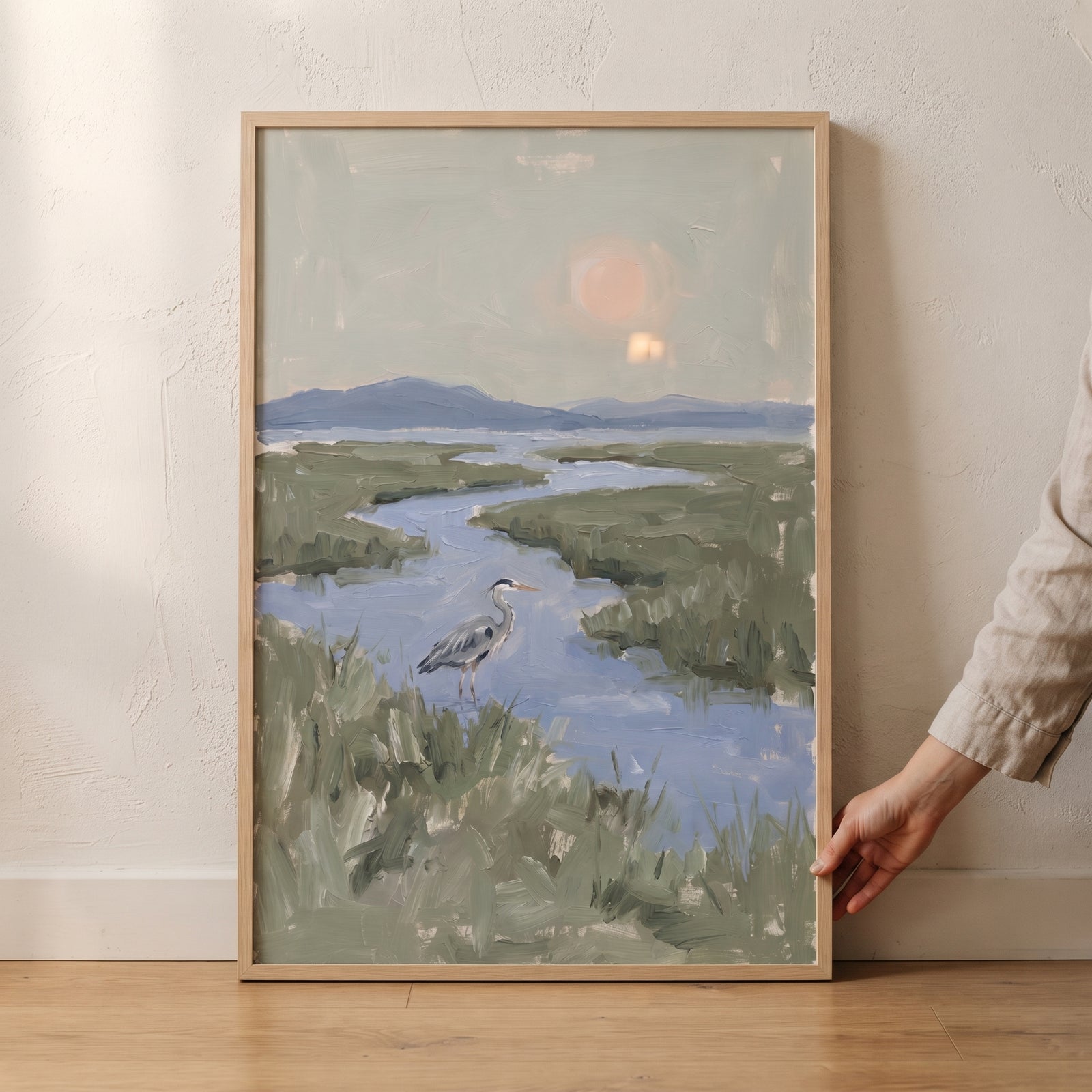 Serene marsh grey heron bird wall art depicts the bird standing in a blue winding river among green marshland and hills.