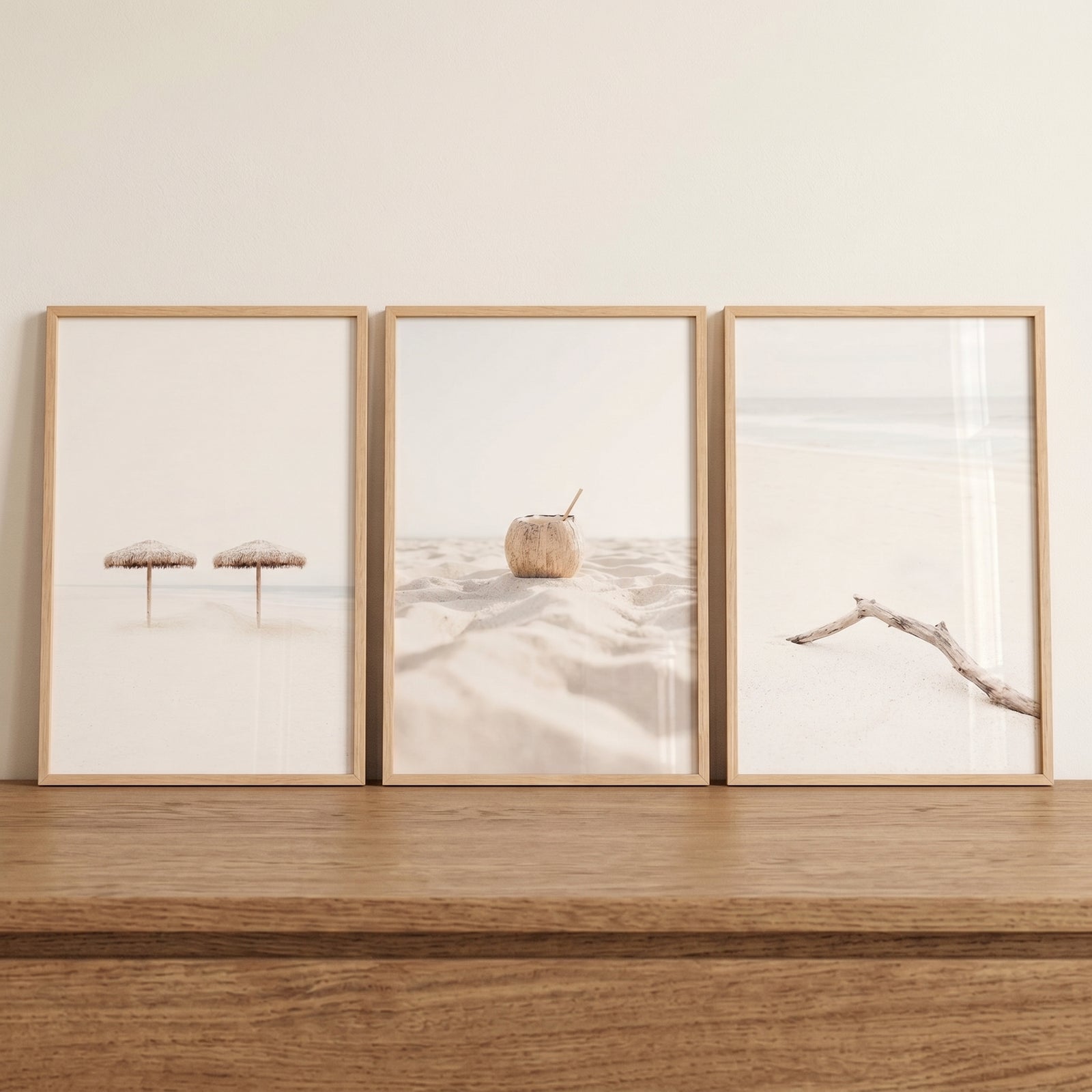 Serene minimalist white beach wall art set of 3 with umbrellas, a coconut, and driftwood in wooden frames on a shelf.