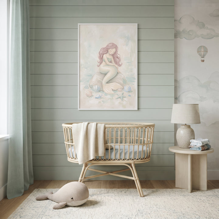 A sage green nursery with a rattan crib, whale plush, and serene pink hair mermaid wall art centered on a paneled wall.