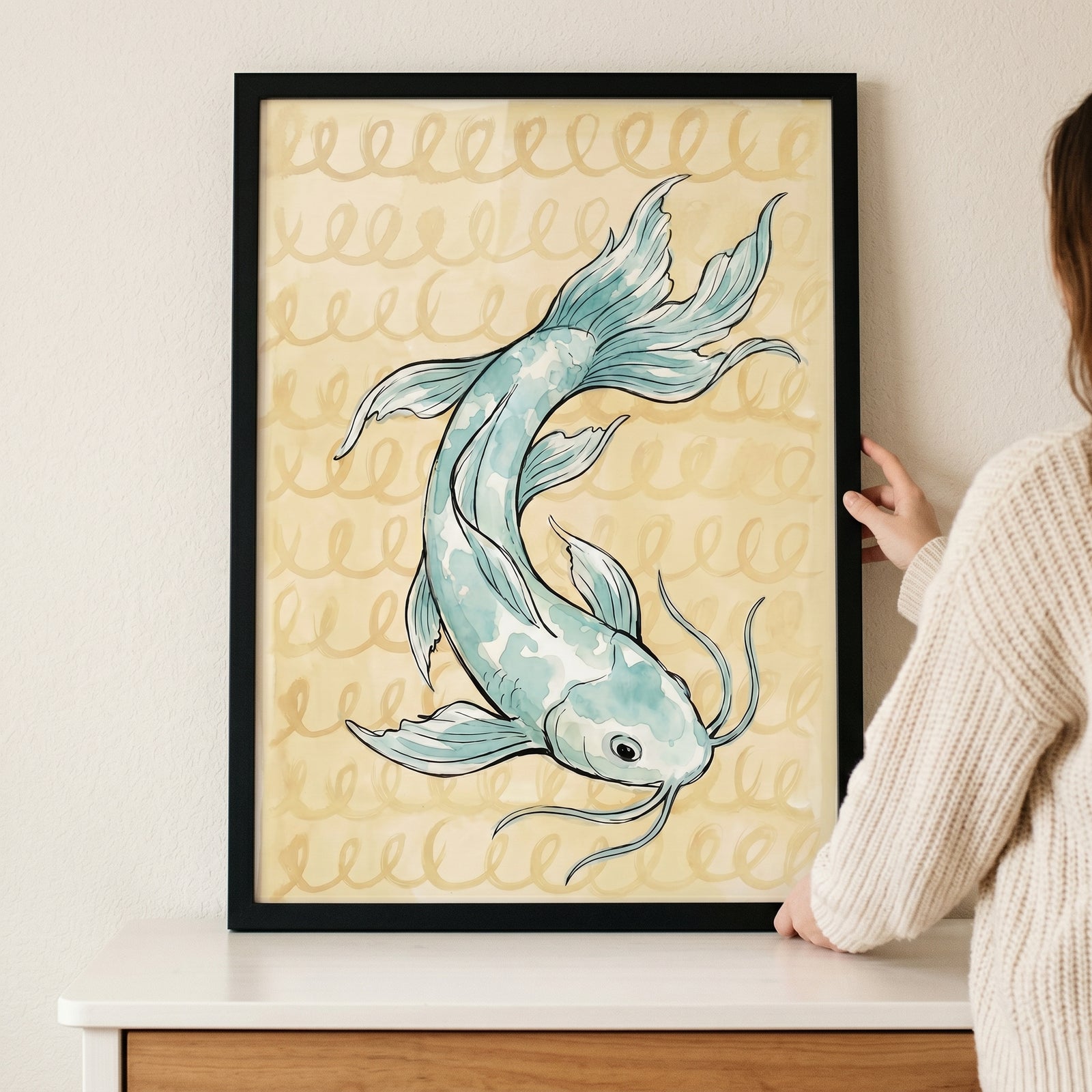 Serene watercolor blue koi fish wall art in a black frame, held against a wall by a person in a knit sweater.