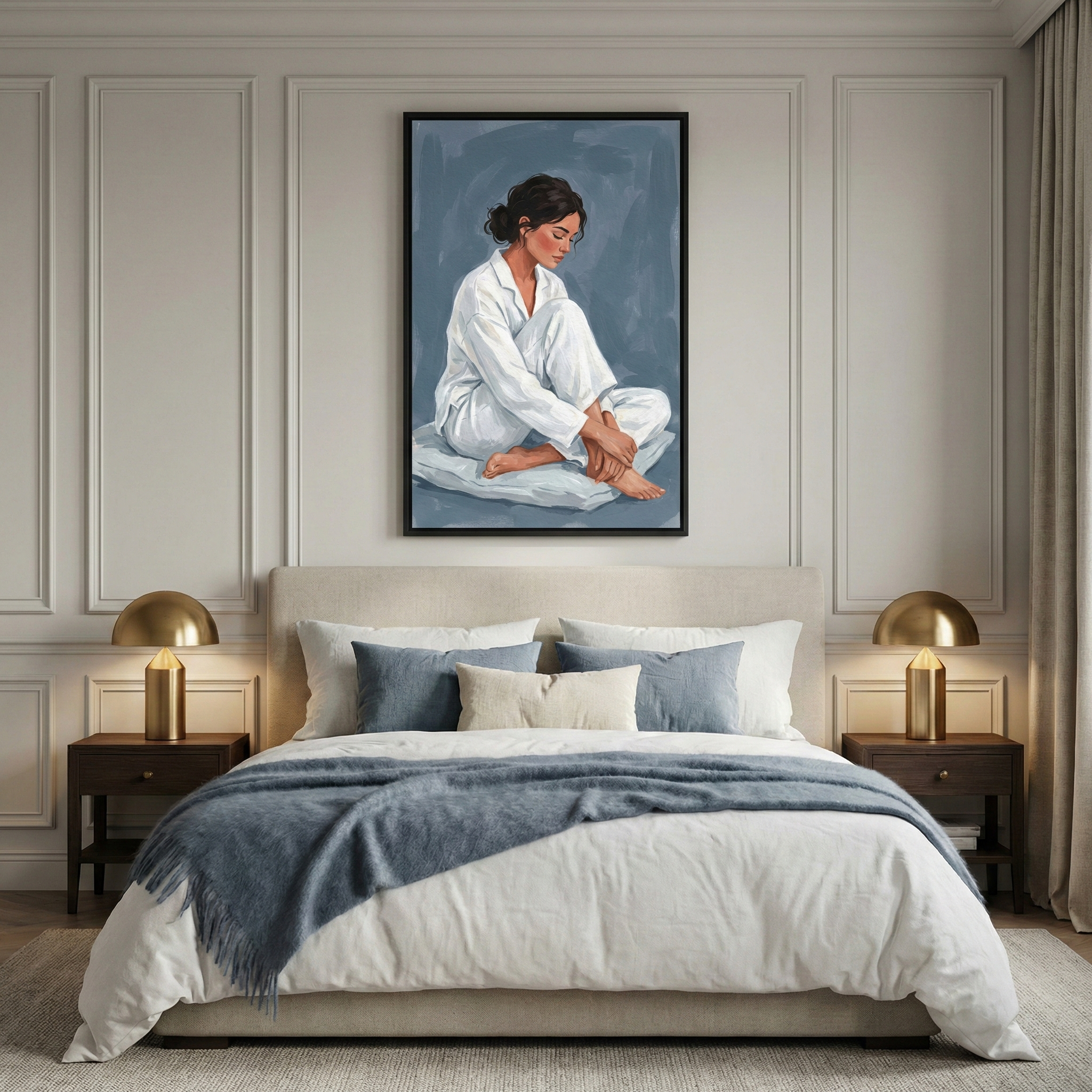 A serene and elegant bedroom featuring light gray paneled walls. A large bed is centered in the room, styled with white linens, several accent pillows in shades of blue and cream, and a textured blue throw blanket. On each side of the bed stands a dark wood nightstand topped with a modern, gold dome-shaped lamp. Above the bed hangs a large, framed illustration of a woman with dark hair wearing white loungewear, sitting in a contemplative pose against a textured dark blue background. 