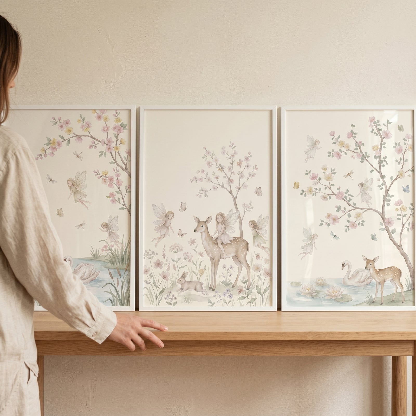 Person stands by a wooden table with a shabby chic blossom fairies wall art set of 3 in soft pastel colors.