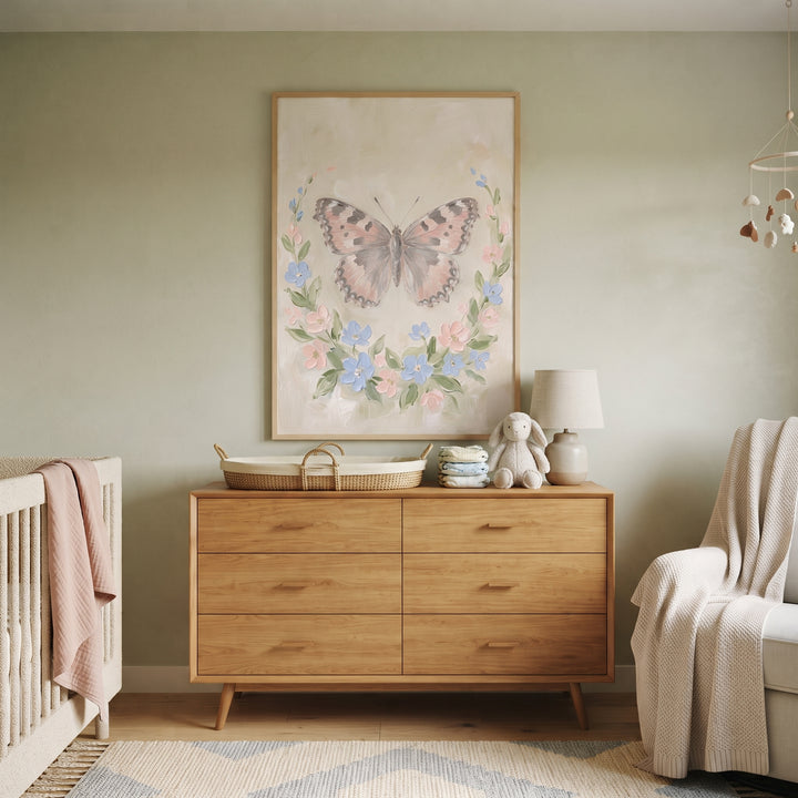 Shabby chic floral butterfly wall art hangs above a wooden dresser in a sage green nursery with a crib and armchair.
