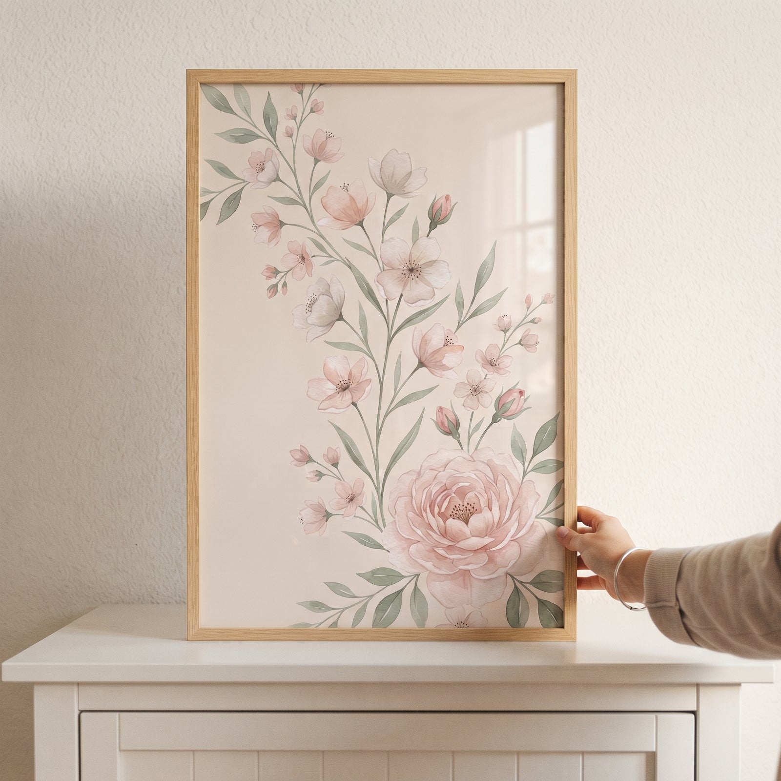 Shabby chic floral wall art with pink blossoms and green leaves in a light wood frame on a white cabinet.