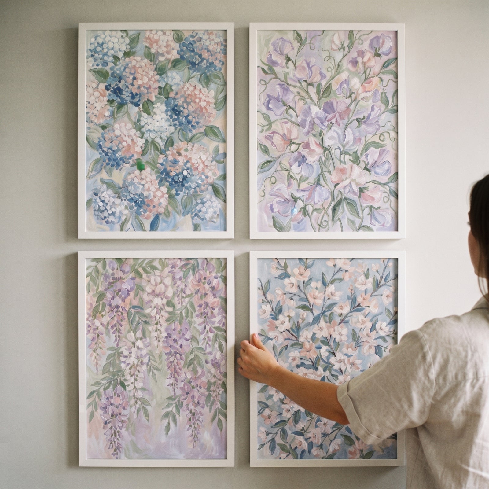 Person adjusts a shabby chic garden floral wall art set of 4 featuring pastel blooms in white frames on a neutral wall.